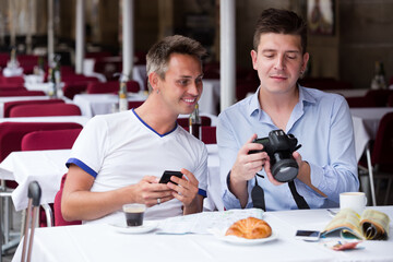 Smiling men sitting with coffee and looking photos at the table