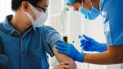 Young Asia lady nurse giving Covid-19 or flu antivirus vaccine shot to senior male patient wear face mask protection from virus disease at health clinic or hospital office. Vaccination concept. - obrazy, fototapety, plakaty
