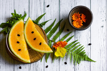 Sweet yellow water melon slices with seeds and flowers, top view