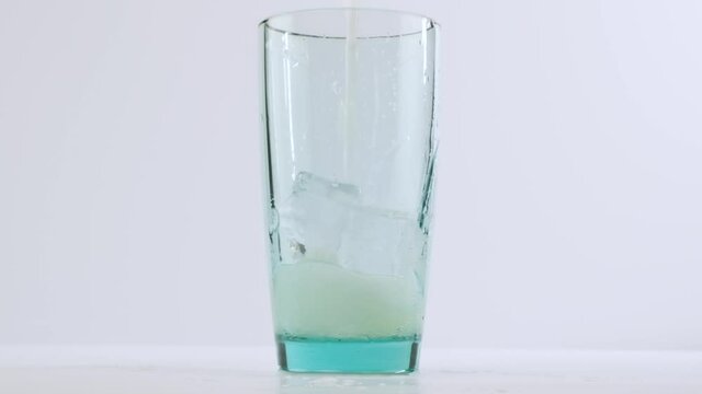 Fresh lemonade pouring into glass standing on white table top in slow motion