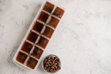 Cubes of frozen coffee in the form of ice on a light gray stone background. Coffee beans.