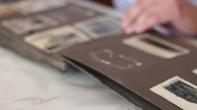 Man flips through the pages of an old album and looks through photographs.