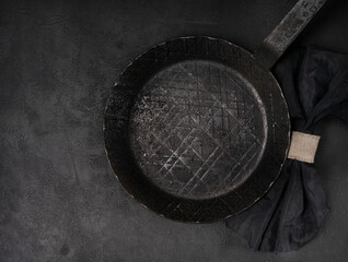Vintage forged empty carbon steel frying pan, with napkin on black background, top view.