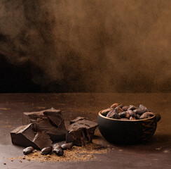 pieces of chocolate in a bowl with airy cocoa powder on a dark brown table