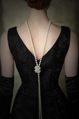 Beautiful female figure from the back in a black dress and pearls in the style of 20-30 years of...