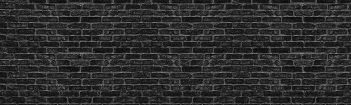 Wide old black shabby brick wall texture. Dark rough masonry panorama. Brickwork panoramic grunge background