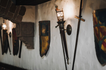 Shields, swords and a torch-shaped wall lamp. Medieval concept and knightly elements.
