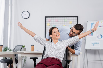 businessman behind excited businesswoman with outstretched hands on chair