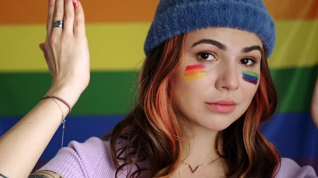 A happy playful young woman is posing to the camera standing isolated over rainbow flag