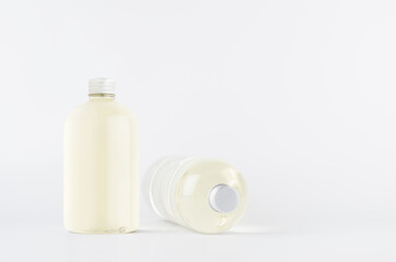 Set of two transparent plastic low thick bottles standing and lying with pale fresh drink or cosmetic essential oil and silver cap, mockup on white background,  front and side view.