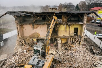 Yellow excavator destroys building. Heavy duty machine is demolishing a brick building. Demolition...