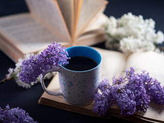 Obraz na płótnie Canvas A cup of coffee and an old book on the table with blooming branches of purple and white lilacs. Vintage Greeting Card