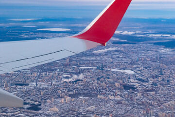 Naklejka na ściany i meble a view of the winter city from a height of flight from the window of an airplane with a silvery red wing