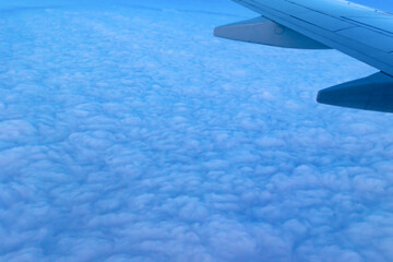 view of the blue cloudy sky from the height of flight above the clouds from the airplane window. part of an airplane wing in the frame