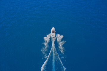 Top view of a white boat sailing in the blue sea. luxury motor boat. Drone view of a boat sailing at high speed. Aerial view of a boat in motion on blue water.