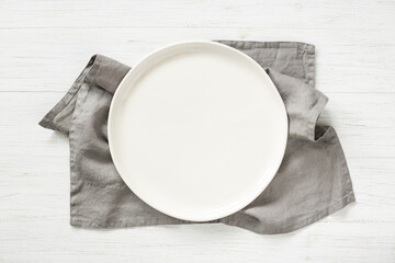 White empty plate with gray napkin on wooden table. Top view.