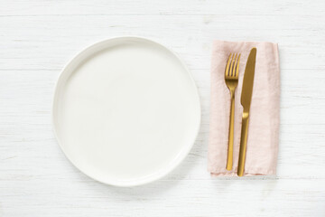 White empty plate and golden cutlery with pink napkin on wooden table. Top view on table setting.