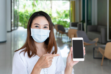Smiling young Asian woman with protective face mask holding smartphone for copy space. New normal, prevent pollution and disease concept