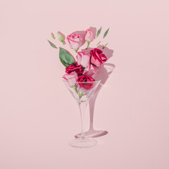 Romantic Valentine's Day composition made with cocktail glass, green leaves and pink roses on pastel background. Minimal flat lay.