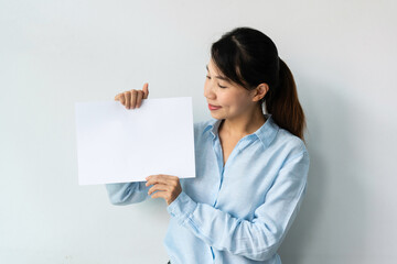 Beautiful young Asian woman in blue shirt holds a blank sheet of paper in hands for advertisement isolated over white background. Copy space.