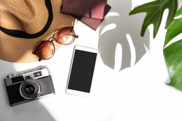 Flat lay of summer accessories with green tropical leaf and shadow on white desk. Summer, holiday and planning travel concepts. Top view and copy space.
