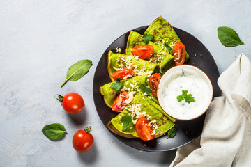 Green pancakes from spinach with cheese and tomatoes and yogurt dressing. Top view with copy space.