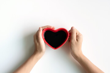 Flat lay of heart shaped cup of black coffee in the hands of women on a white desk with copy space. top view. Valentine, lifestyle concept