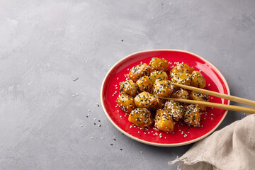 Traditional сhinese fried apples in caramel with sesame seeds on red vintage plate with chopsticks on gray background, space