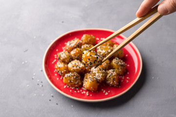 Traditional сhinese fried apples in caramel with sesame seeds on red vintage plate with chopsticks...
