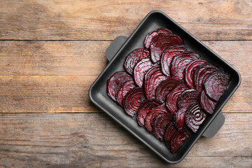 Baking dish with roasted beetroot slices on wooden table, top view. Space for text