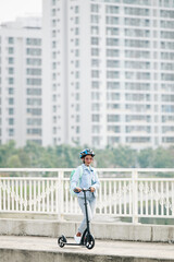 Attractive young Asian woman in jeans and denim jacket riding on bridge and looking at camera