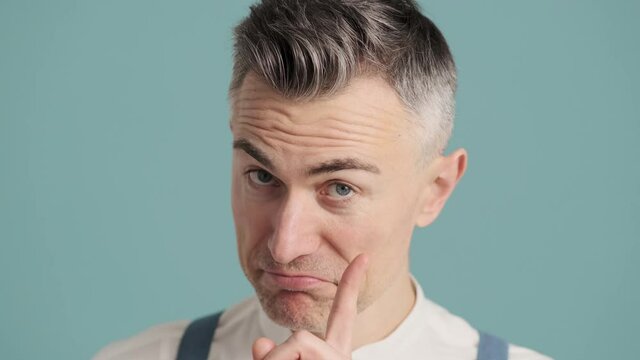 A close-up view of an attractive man is doing secret gesture while standing isolated over blue background wall