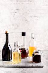 Original glass bottles with different vinegar on a marble table against a background of a white brick wall. Copy space.