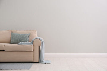 Comfortable beige sofa near light wall indoors, space for text. Simple interior