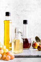 Original glass bottles with different vinegar on a marble table against a background of a white brick wall. Copy space.