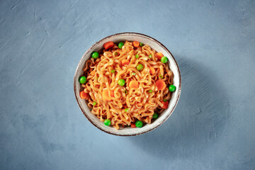 Noodles with vegetables in a bowl, overhead shot on a blue background
