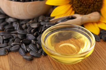 Sunflower oil in glass bowl and seeds on wooden table, closeup
