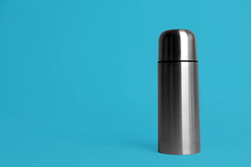Stylish thermo bottle on light blue background, space for text