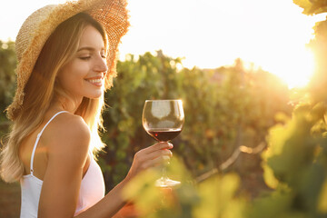 Beautiful young woman with glass of wine in vineyard on sunny day - Powered by Adobe