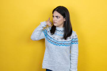 Young caucasian woman wearing casual sweater over yellow background confused doing phone gesture with hand and fingers like talking on the telephone