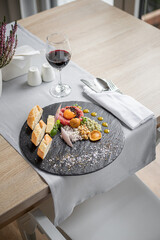 Piękny marmurowy talerz udekorowany jedzeniem, grzankai złocistymi, kolorowymi krewetkami owocami morza, kieliszek wina sztućce w serwecie elegancjiej oraz przyprawnik.