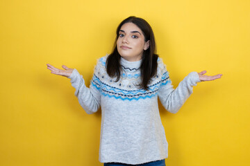 Young caucasian woman wearing casual sweater over yellow background clueless and confused expression with arms and hands raised