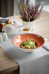 Sałatka w pięknym ozdobnym talerzu, podane na stole w restuaracji dodatkami są wypolerowane błyszczące srebrne sztućce, herbata oraz serwetki i laweda. Sałatka z ziołami i sosem białym.