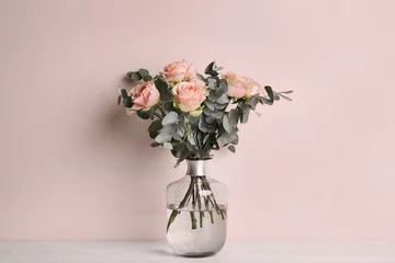Foto auf Glas Vase with bouquet of beautiful roses on white wooden table near beige wall © New Africa