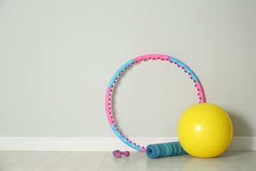 Hula hoop, exercise ball, yoga mat and dumbbells near light wall in gym. Space for text © New Africa