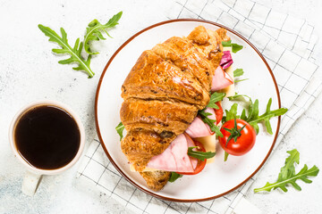 Croissant sandwich with ham, cheese and fresh salad with cup of coffee. Healthy breakfast. Top view with copy space on white stone table.