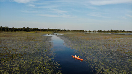 Aerial view of young man floats on an orange kayak on the overgrown river. Ukraine, Europe