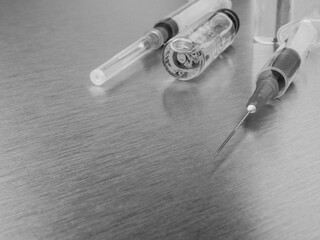 Syringes and ampoules on a polished metal background. Coronavirus vaccination and immunization concept. Selective focus. Black and white monochrome image. Copy space.