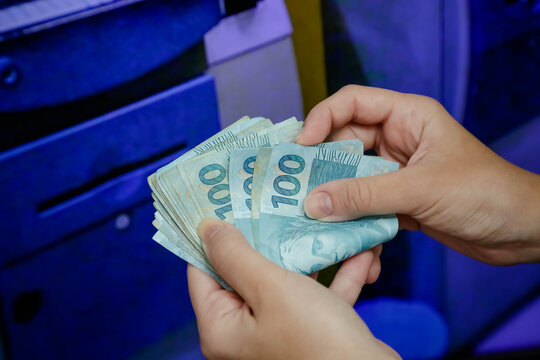 Mulher segurando cedulas de 100 reais  com fundo desfocado.
