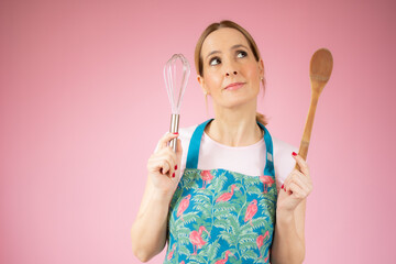 Beautiful young woman holding kitchen utensils over pink background.